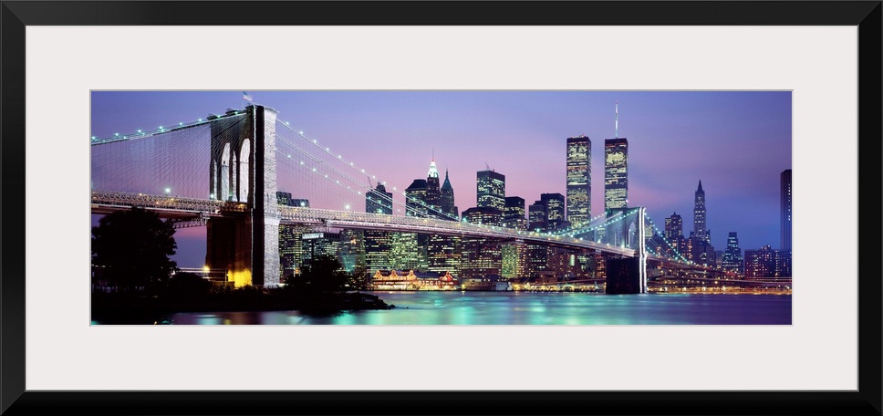 Large panoramic view of the Brooklyn Bridge lit up at night.  The waters of the East River reflecting the Manhattan skylin...