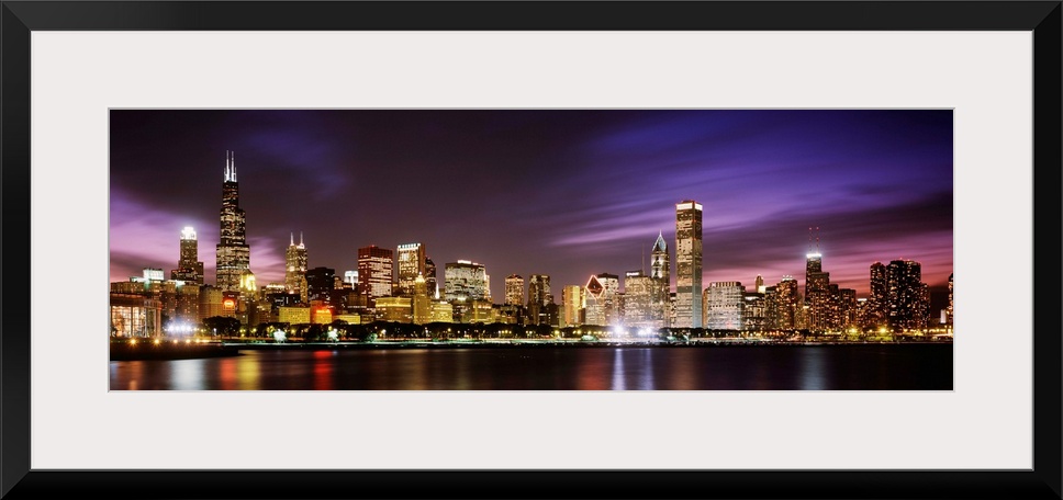 A big cityscape panoramic of downtown Chicagoos lights reflecting off Lake Michigan at night.