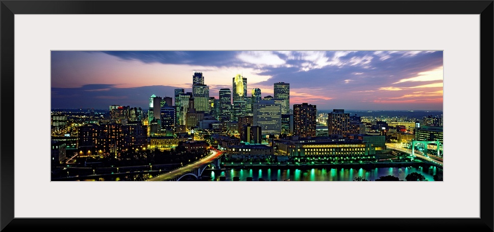 Wide angle panoramic photograph of Minneapolis skyscrapers at night, beneath a colorful sunset.
