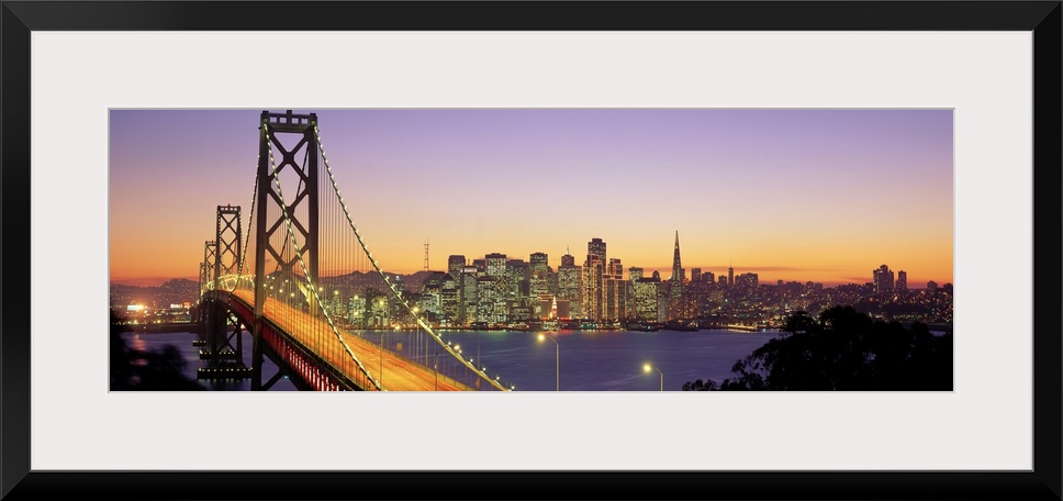 Twilight and the Golden Gate Bridge with the San Francisco Skyline with a purple and gold sky.