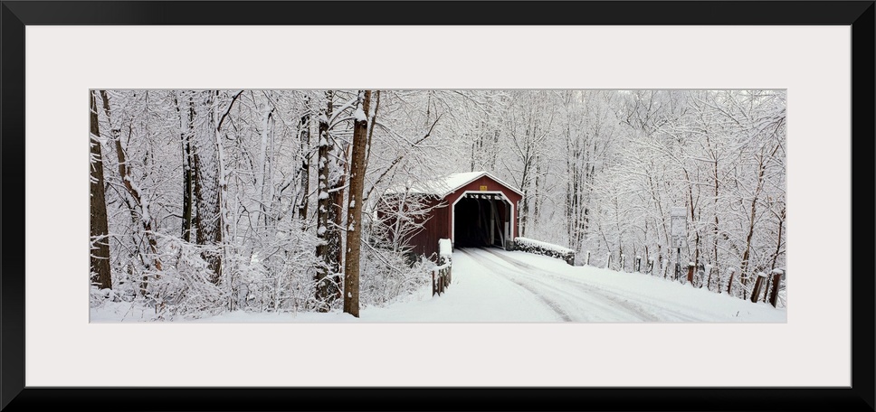 Panoramic photograph of a snow covered bridge in Pennsylvania that is surrounded by a forest.