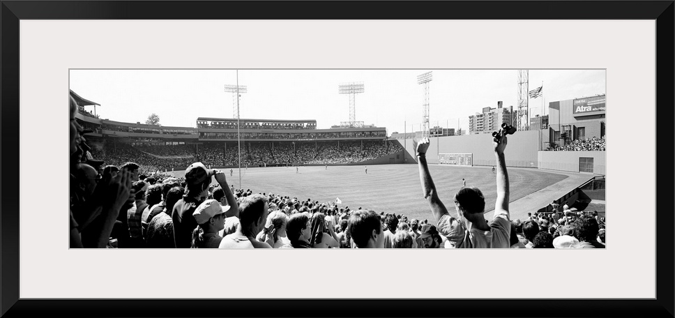 Big, panoramic black and white photograph of Fenway Park in Boston, with fans standing and cheering in the foreground.