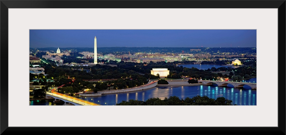 Panoramic photograph of the nation's capital at night with bright lights reflected in the water.  The Washington Monument ...