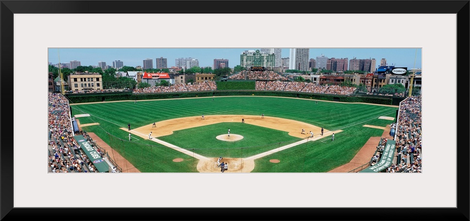 Panoramic photograph of Wrigley Field with Chicago skyline in the distance.  Stadium is full of people and the players are...