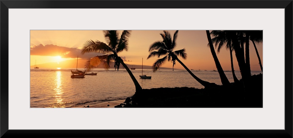 Panoramic photograph of a colorful sunset in the town of Lahaina on the island of Maui in Hawaii.  The bright sun shines o...