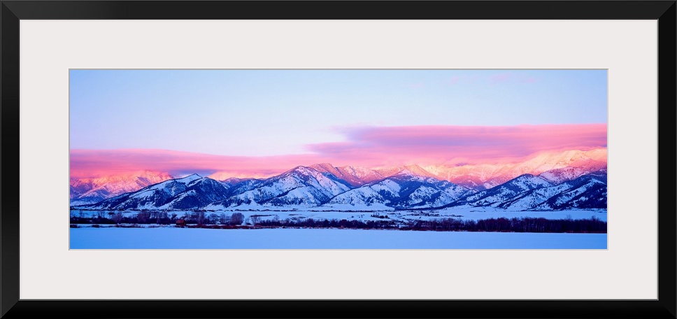 A panoramic snowscape photograph of plains and clouds passing over mountains at the end of the day.
