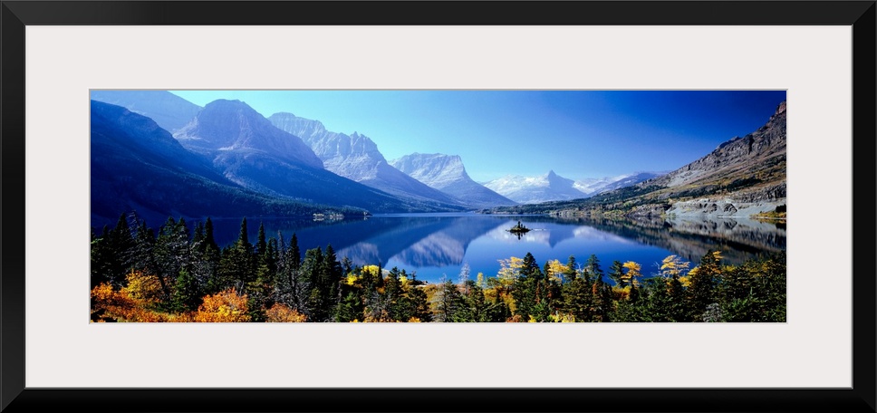 A panoramic photograph of mountains reflecting in a still lake surrounded by trees in this landscape of the wilderness.