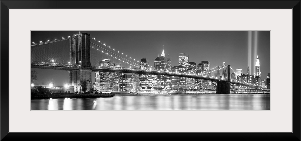 A panoramic landscape photo taken after 2001 of Manhattan and Brooklyn Bridge shining bright over the East River at night.