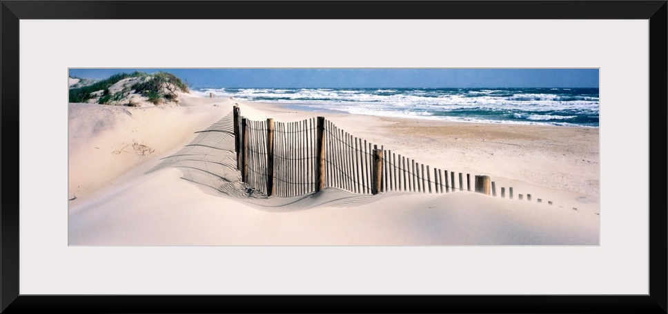 A wooden fence separates sand dunes from the Atlantic Ocean in this panoramic image.