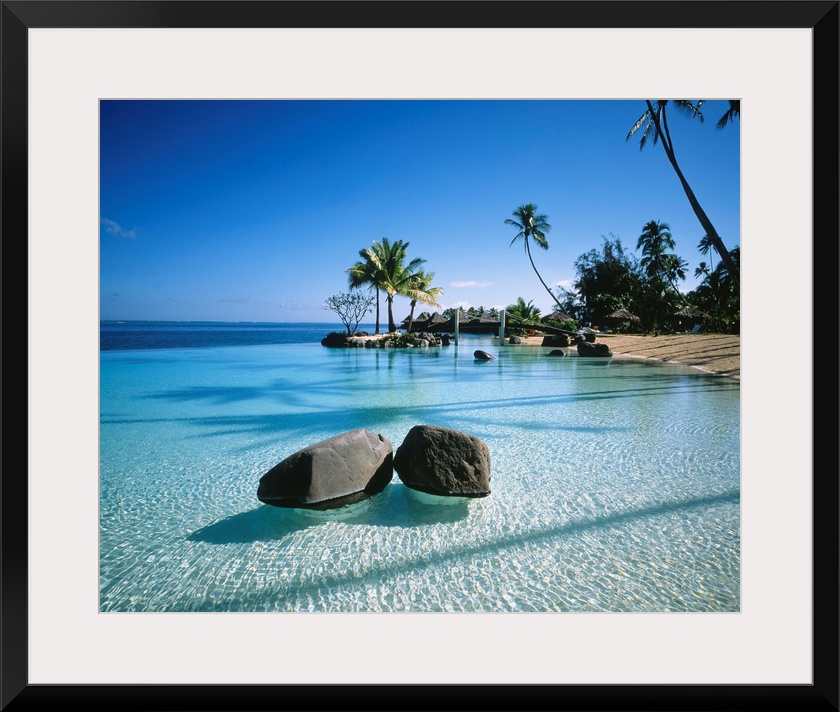 Large landscape artwork for a living room or office of clear water ripples around rocks on a tropical beach lined by palm ...