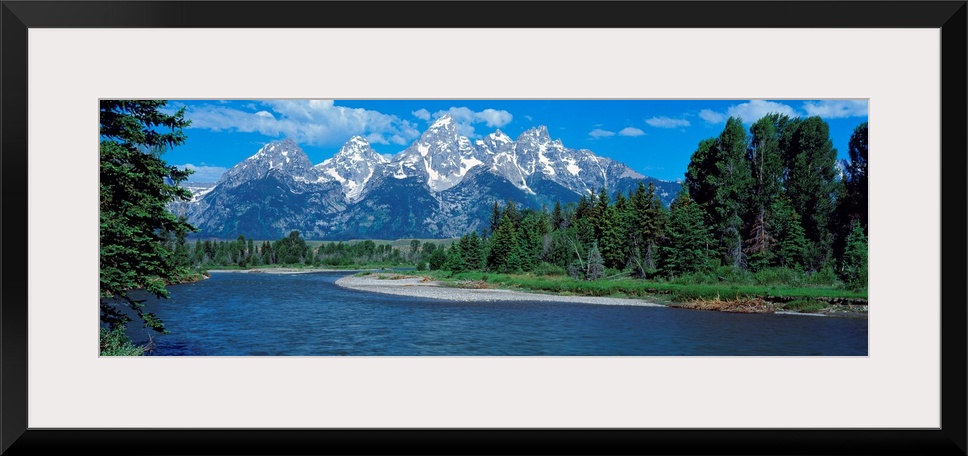 Panoramic photo of rugged mountains in the background of a wide river cutting through the landscape with trees on either s...