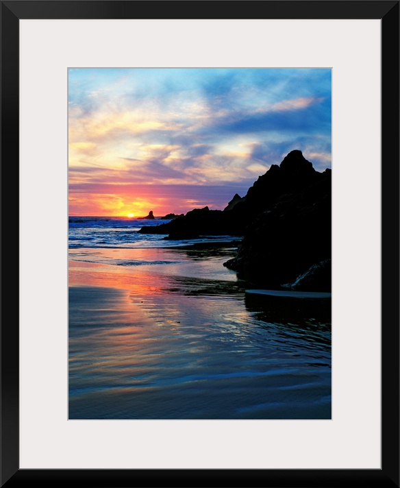 Sun below the horizon in a seascape with a rocky beach and waves.