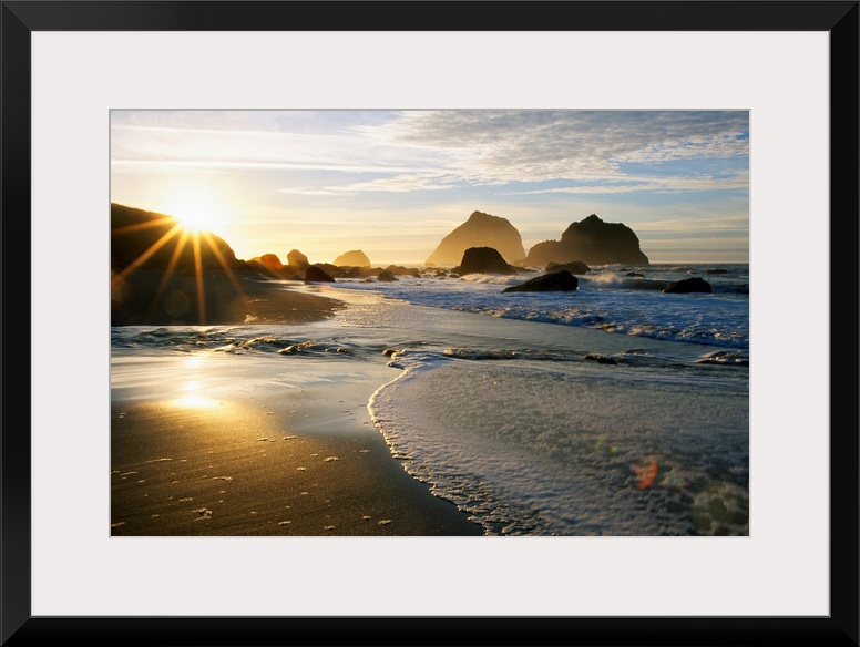 Panoramic photograph displaying a sunset over an ocean and sandy beach.  In the background you can see the waves hitting l...