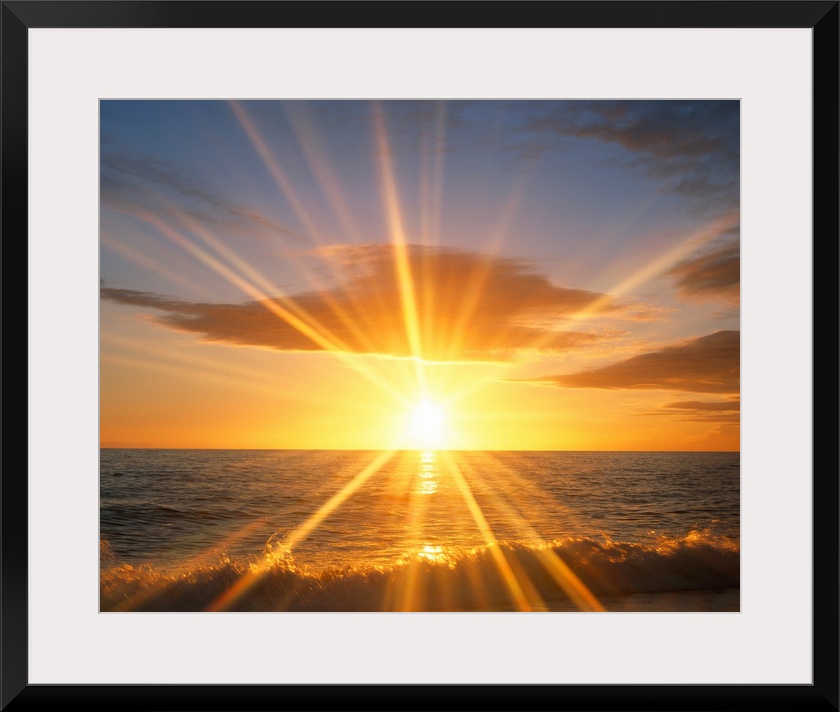 Giant photograph of a bright sunset reflecting onto an ocean as the waves crash against a sandy beach.