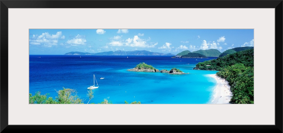 Panoramic photograph of a couple boats sitting in the clear waters of Trunk Bay in the Virgin Islands.  The mountains in t...