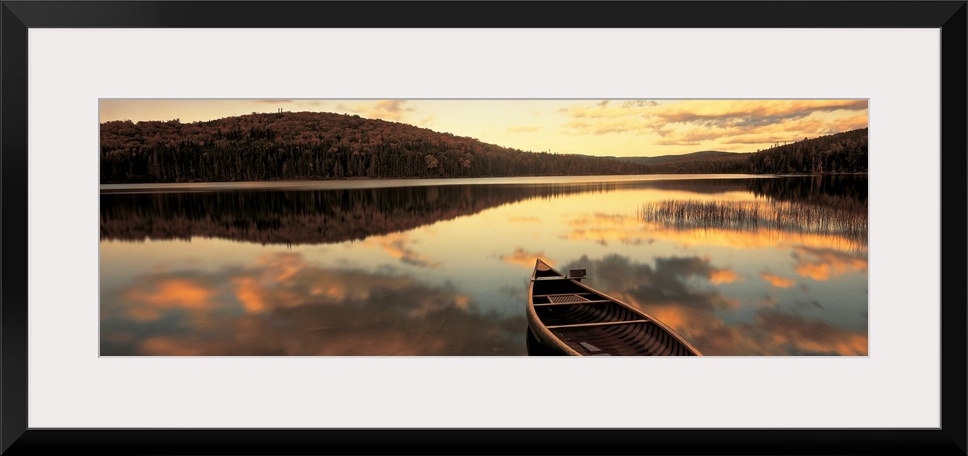 A canoe floats in a still lake at sunset in New England as clouds reflect in the water.