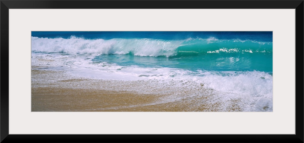 Panoramic photograph of water crashing onto the sand and being swept back out to sea.