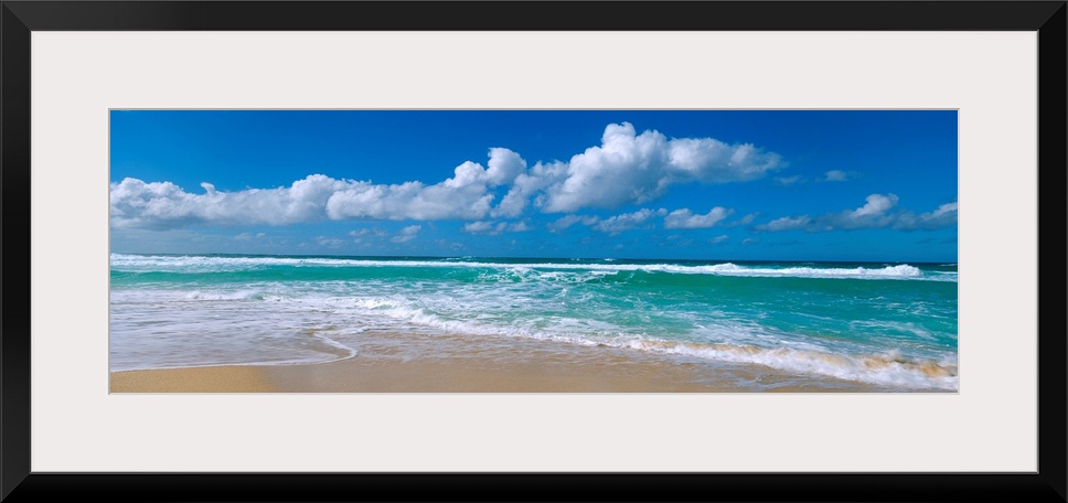 Panoramic view of a Hawaiian beach where waves are washing up on the shore while the wind blows cumulus clouds across an o...