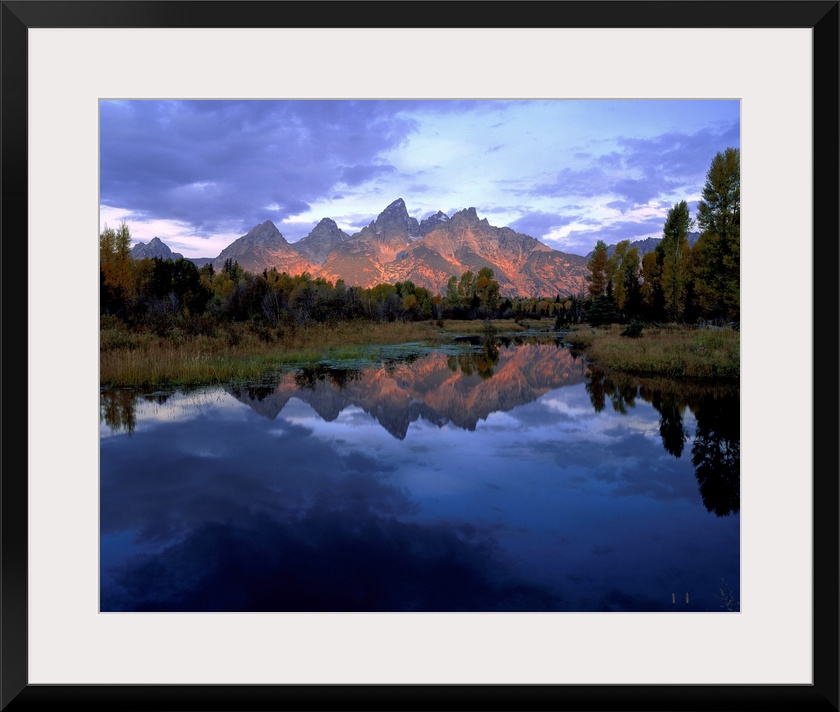 Huge photograph displays a set of jagged mountains in the background as they reflect over the calm water in the foreground...