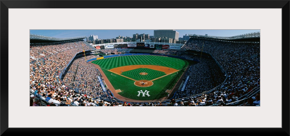 Panoramic photograph taken at Yankee Stadium in the Bronx, New York displays fans enjoying a baseball game on a sunny day....