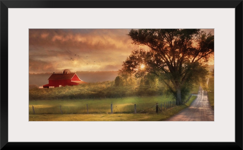 A dirt road in the countryside with a red barn in the distance at sunset.
