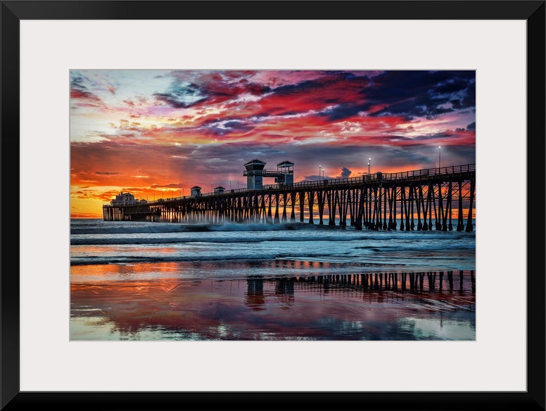 The Oceanside Pier is silhouetted as sunset turns the reflected clouds from yellow to pink to gun metal grey, and finally ...