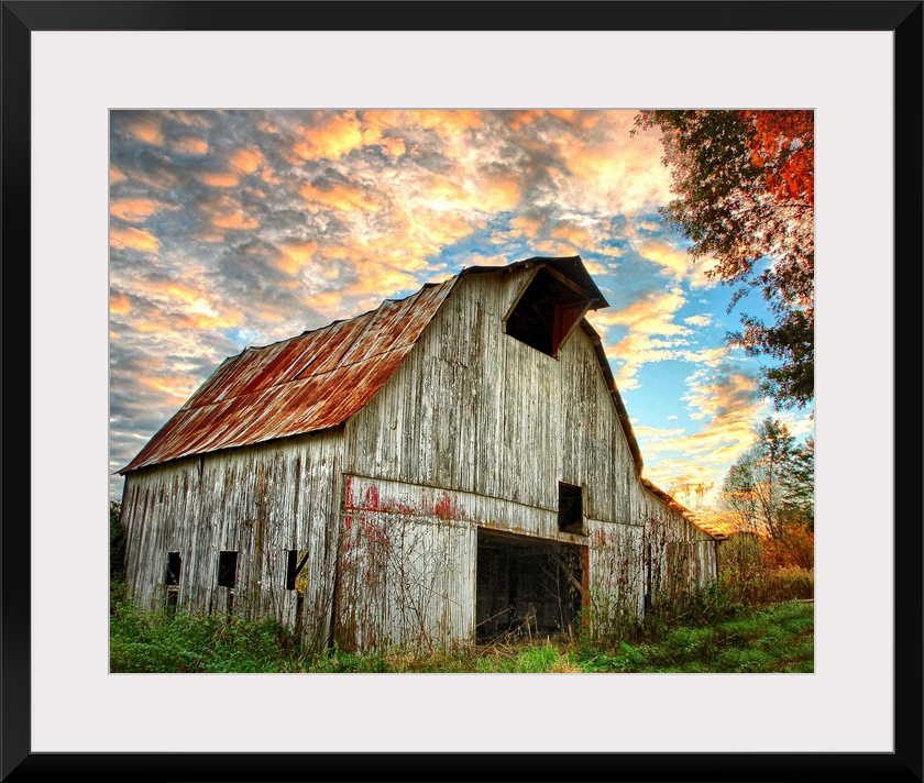 Sunset over an old, weathered barn, with a cloudy sky.