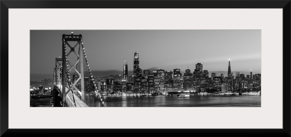 Photograph of the Bay Bridge and the San Francisco skyline lit up at dusk.