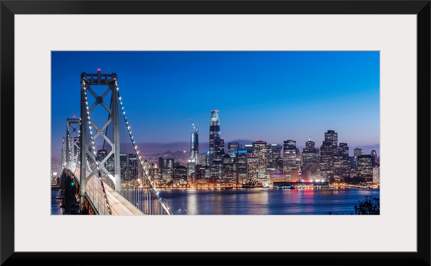 Photograph of the Bay Bridge and the San Francisco skyline lit up at dusk.