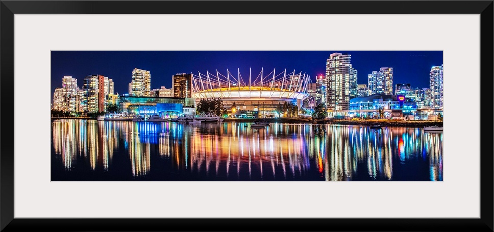 Panoramic photograph of BC Place Stadium and part of the Vancouver skyline lit up at night and reflecting onto the water, ...