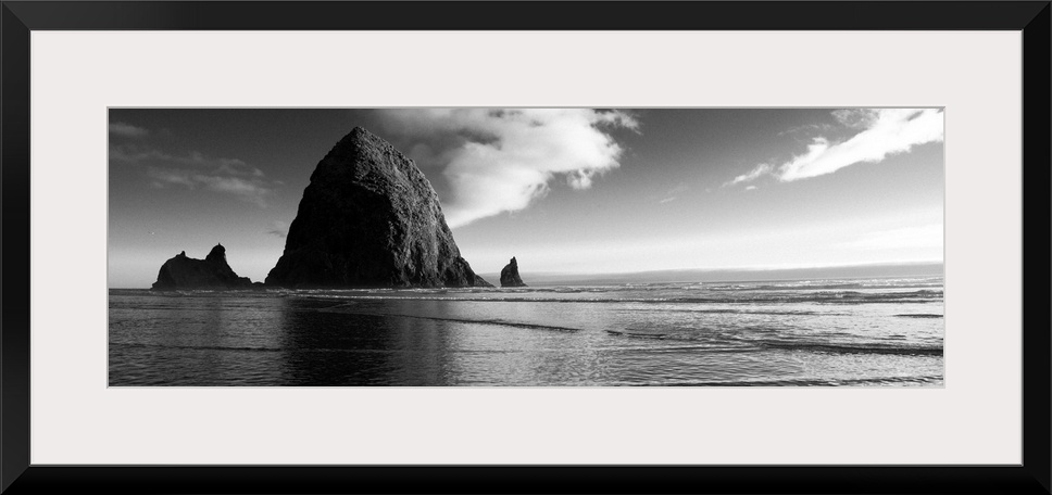 Black and white panoramic photograph of Haystack Rock with rippling waters.