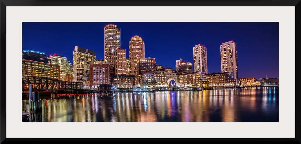 Panoramic view of the Boston City skyline at night, with lights reflected in the water.