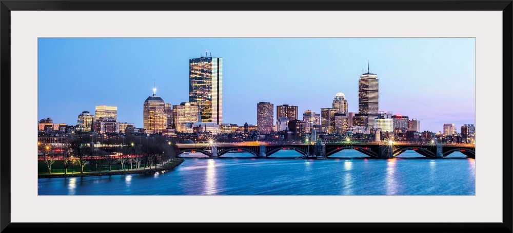 Panoramic view of the Boston City skyline illuminated at night, with the Longfellow Bridge in the foreground.