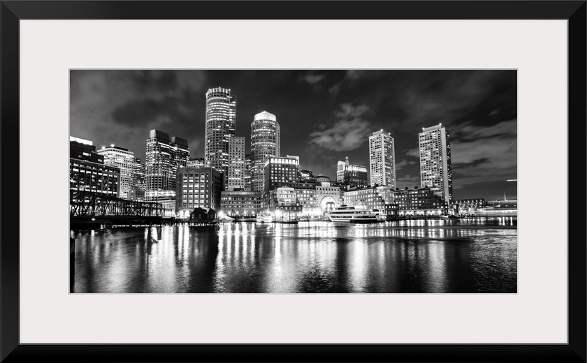 Panoramic view of the Boston City skyline at night, with lights reflected in the water.