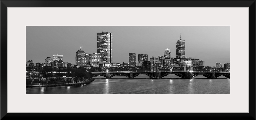 Panoramic view of the Boston City skyline illuminated at night, with the Longfellow Bridge in the foreground.