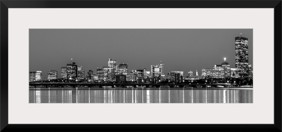 Panoramic view of the Boston City skyline at night, with lights reflected in the water.