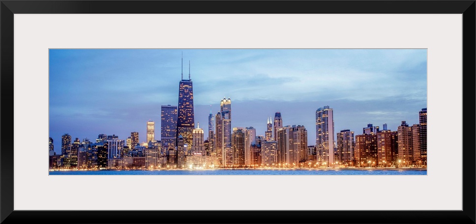 Panoramic view of the Chicago city skyline illuminated in the early evening, seen from the edge of Lake Michigan.