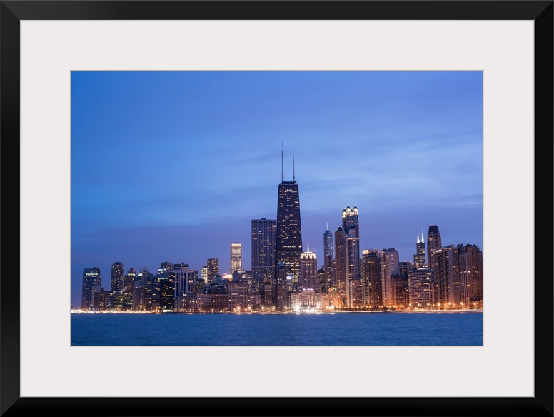 The Chicago city skyline illuminated in the early evening, seen from across the water.
