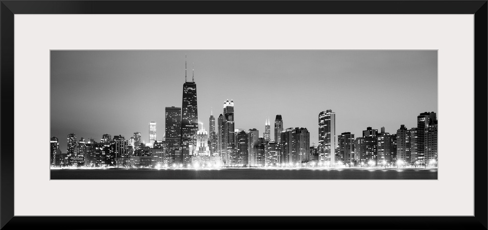 Panoramic view of the Chicago city skyline illuminated in the early evening, seen from across the water.