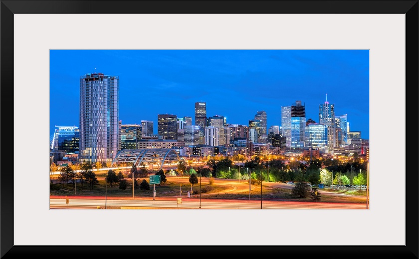 Photograph of the Denver, CO skyline at dusk with warm light trails on the highway from passing cars.