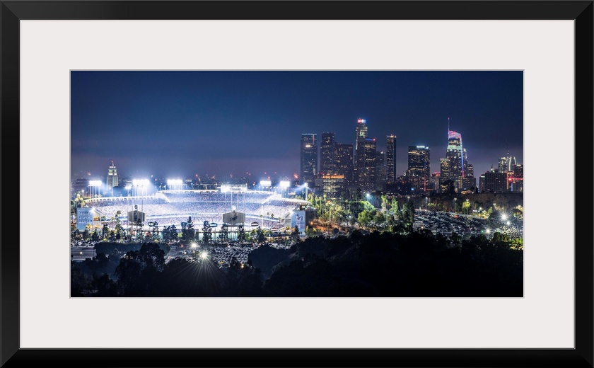 Photograph of Dodger Stadium lit up on a game night with the Los Angeles skyline on the right.