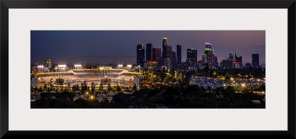 Panoramic photograph of Dodger Stadium lit up on a game night with the Los Angeles skyline on the right.