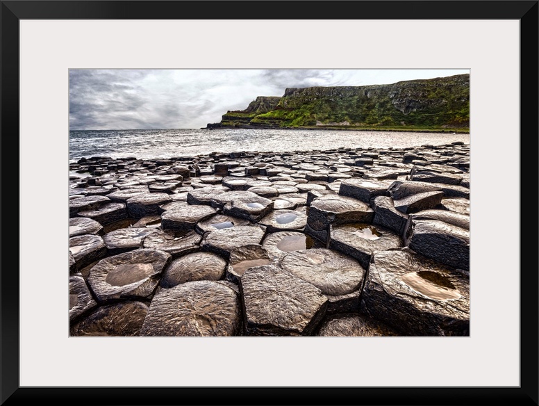 Landscape photograph of the basalt columns on Giant's Causeway with rocky cliffs and the Atlantic Ocean in the background.