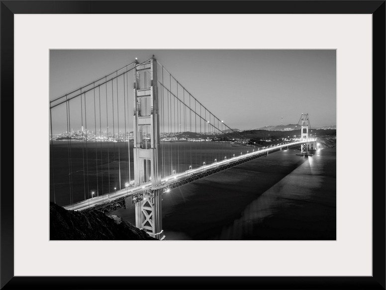 Cool toned photograph of the Golden Gate Bridge lit up at twilight with the city lights in the background.