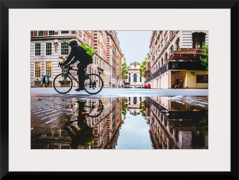 Photograph of a biker reflecting into a puddle in London, England.