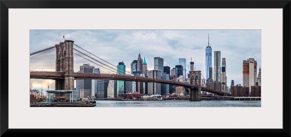 View of the New York City skyline under an overcast sky, with the Brooklyn Bridge, from across the water.