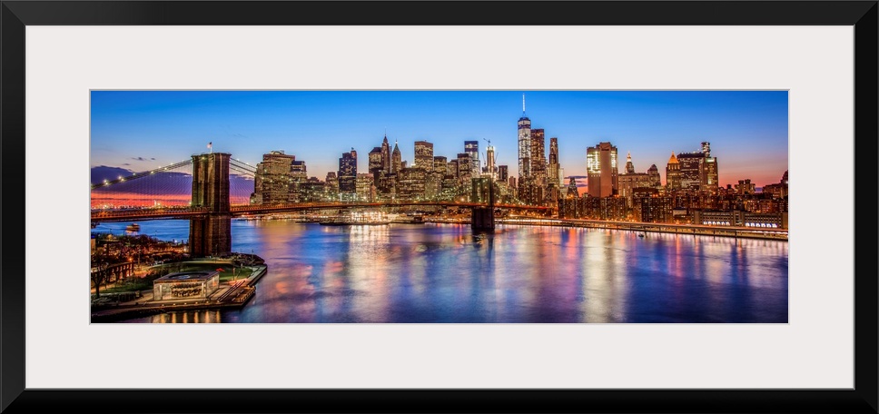 View of the New York City skyline illuminated at night, with the Brooklyn Bridge, from across the water.