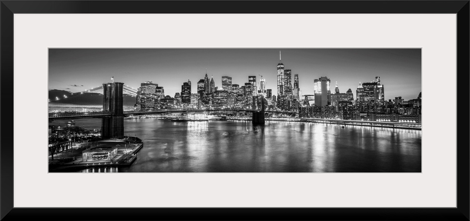 View of the New York City skyline illuminated at night, with the Brooklyn Bridge, from across the water.