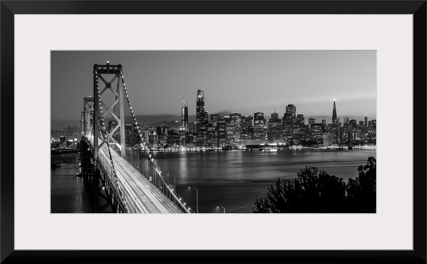 Photograph of the Bay Bridge with a sunset and the San Francisco skyline lit up in the background.