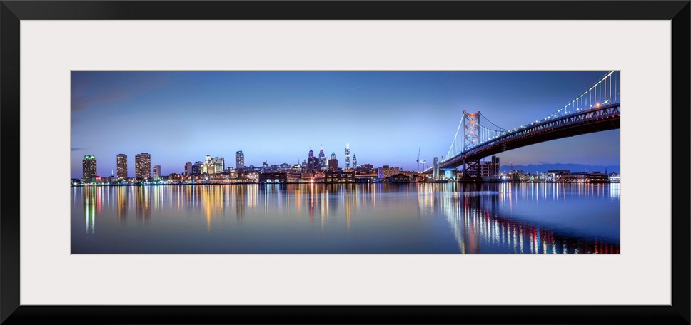 Panoramic photo of the Philadelphia city skyline reflected in the water at night, with the Benjamin Franklin Bridge on the...